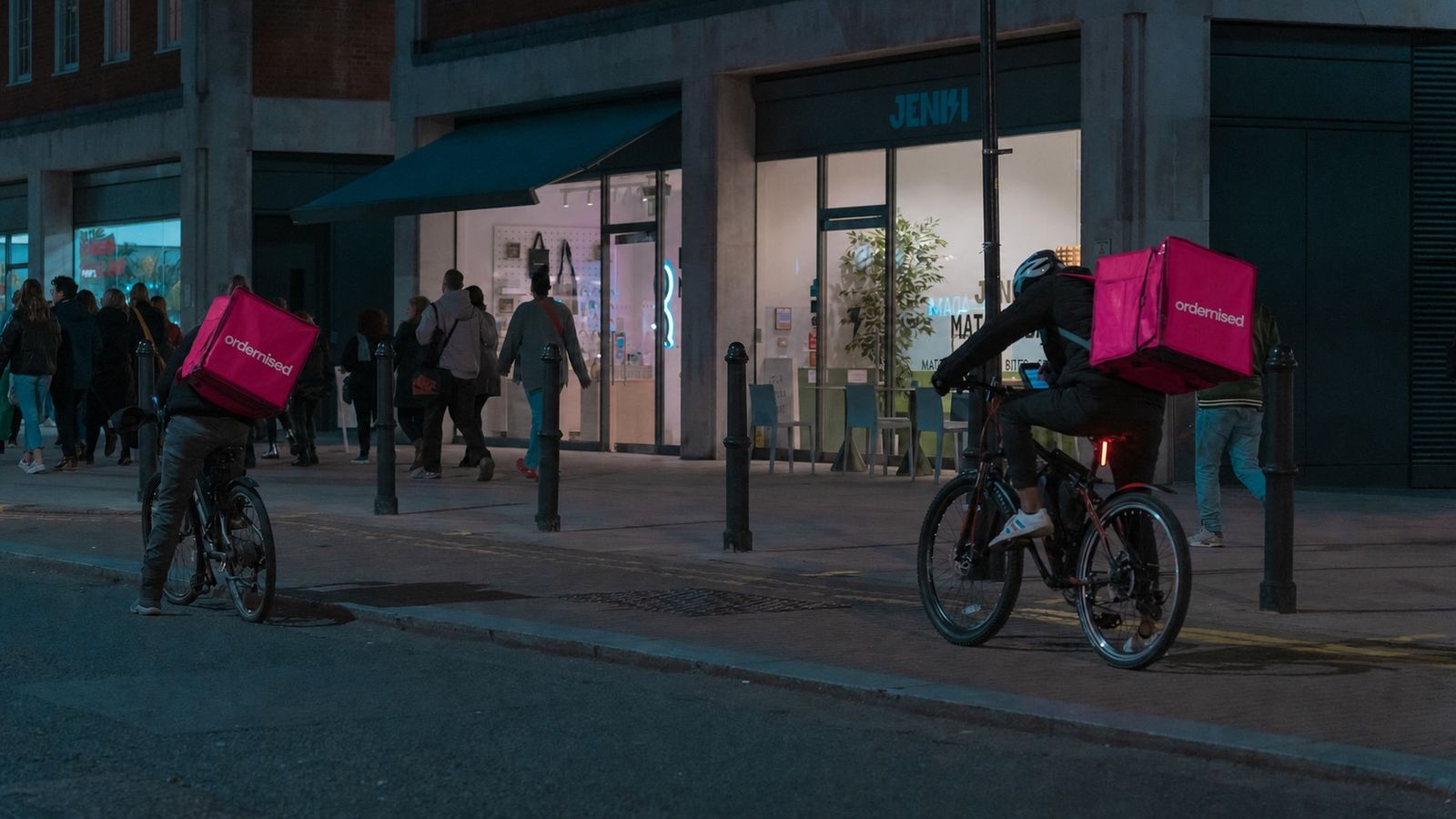 Two riders on a city street at dusk carrying Ordernised delivery boxes
