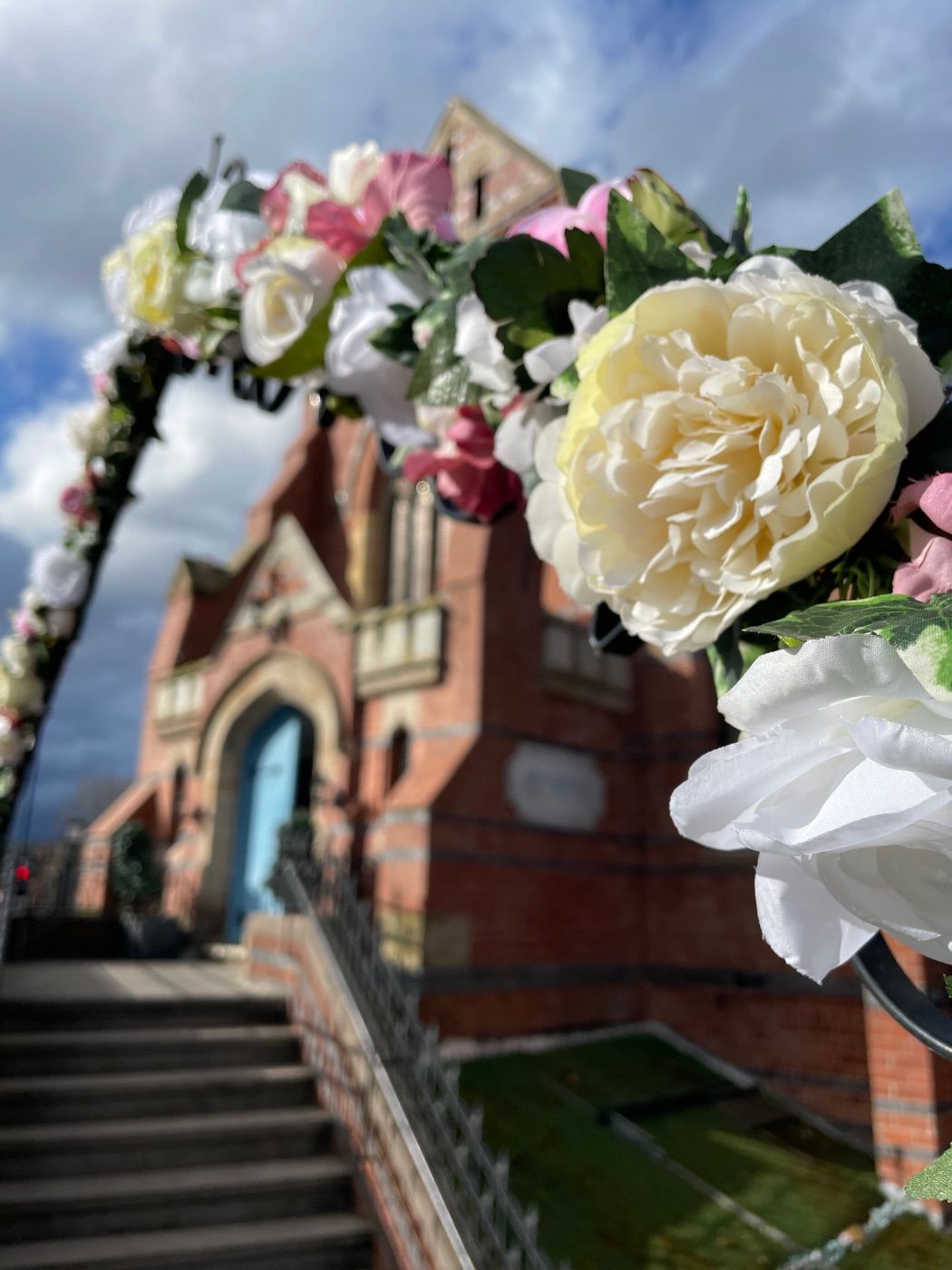 The red brick Victorian exterior of Springfield Hall, framed by a floral wedding arch over the entrance steps